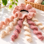 Blush crochet scrunchie with long cream and rose spiral curls on a sunlit white craft table